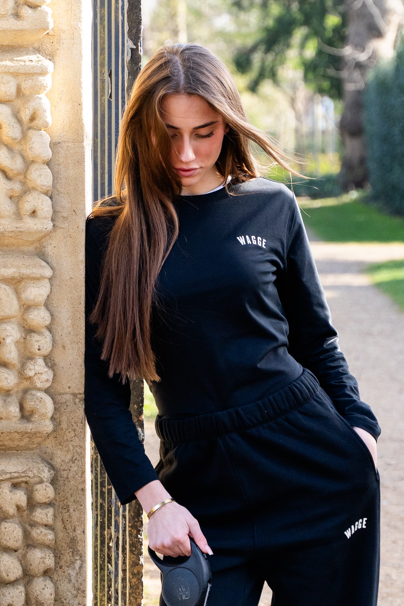 Woman wearing a black long sleeve 'WAGGE' t-shirt with embroidered logo standing outdoors.