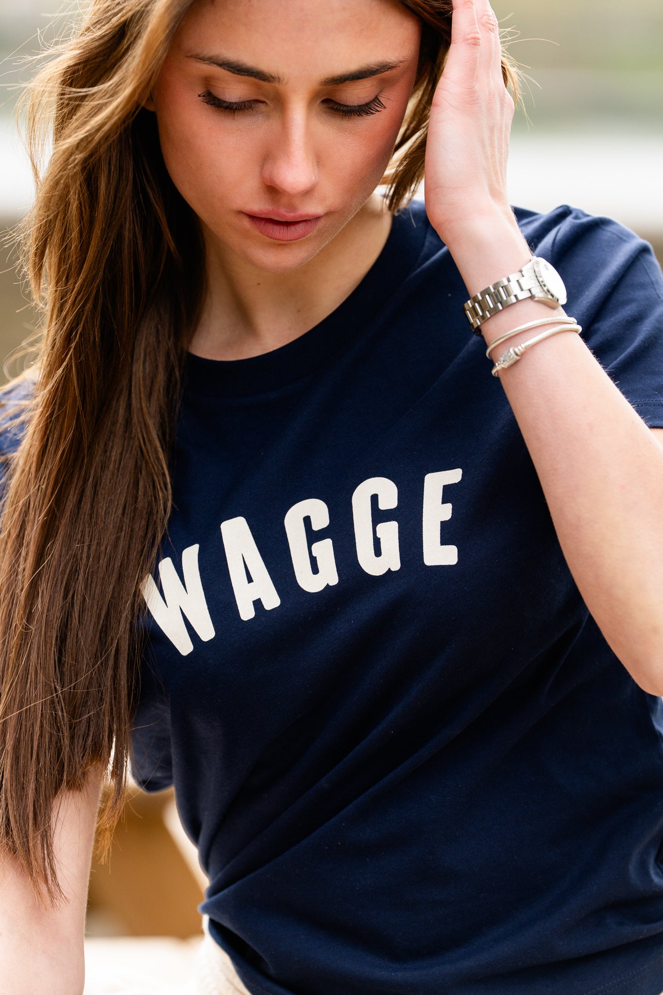 Woman wearing a navy blue t-shirt with 'WAGGE' screen printed logo, outdoors.