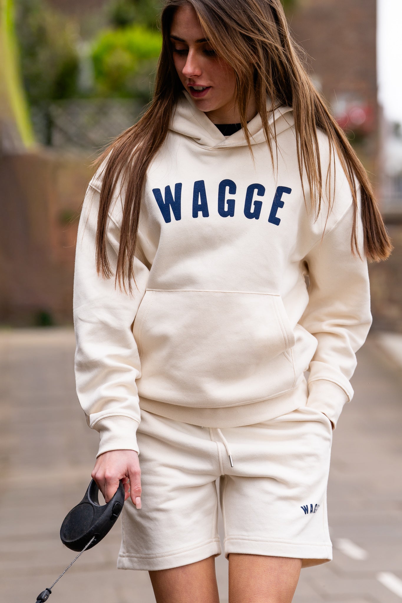 Model wearing raw natural jogger shorts with screen printed 'WAGGE' logo, walking outdoors.
